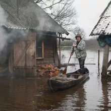 Seto Culture from Voru County, Estonia man standing and paddling wooden boat between houses on lake