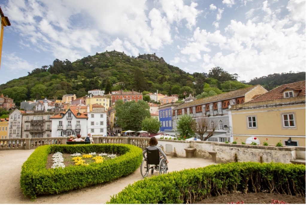 Image of ornamental garden with wheelchair user looking to Sintra traditional buildings and hillside